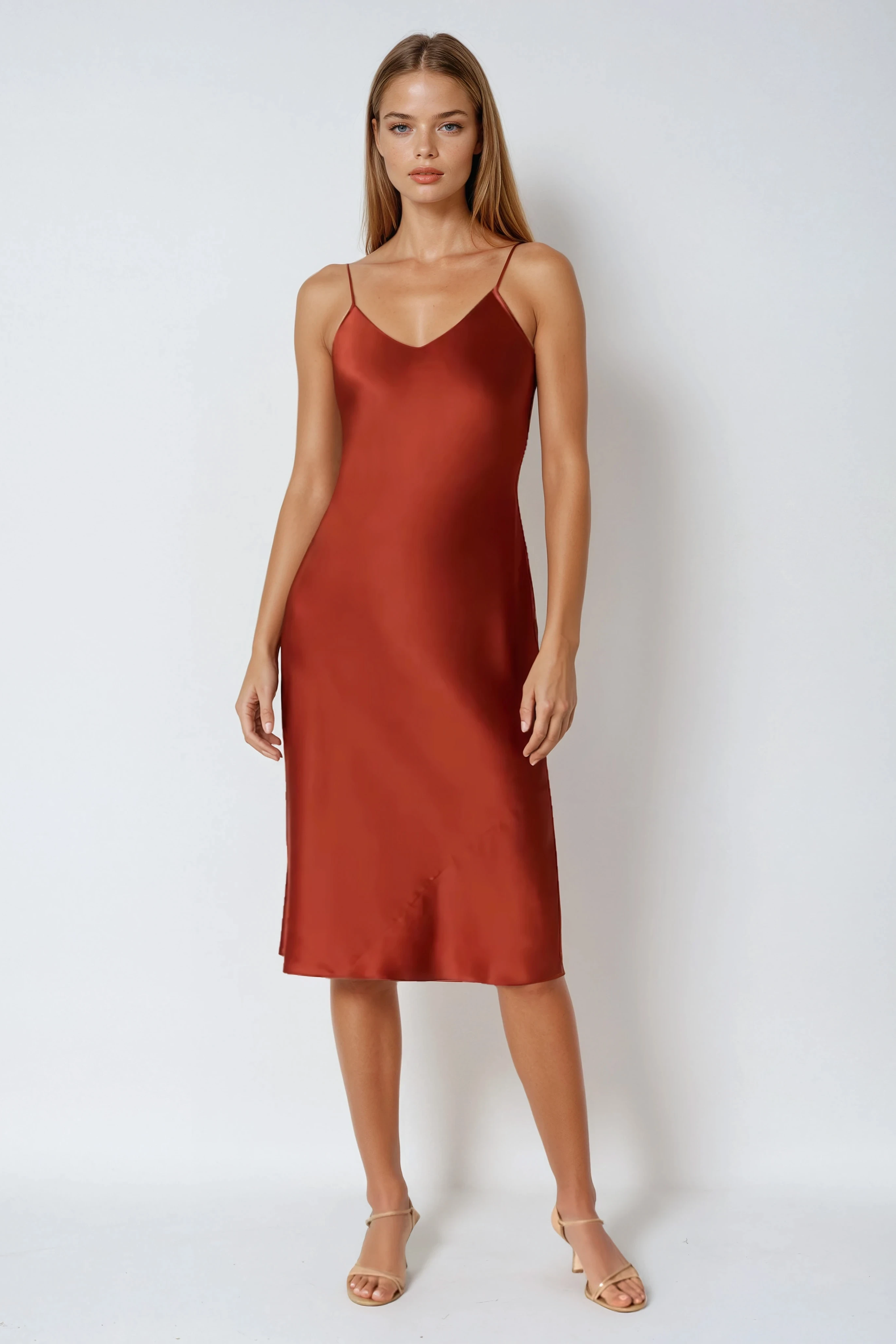 Woman wearing a rust-colored silk satin slip dress against a white background
