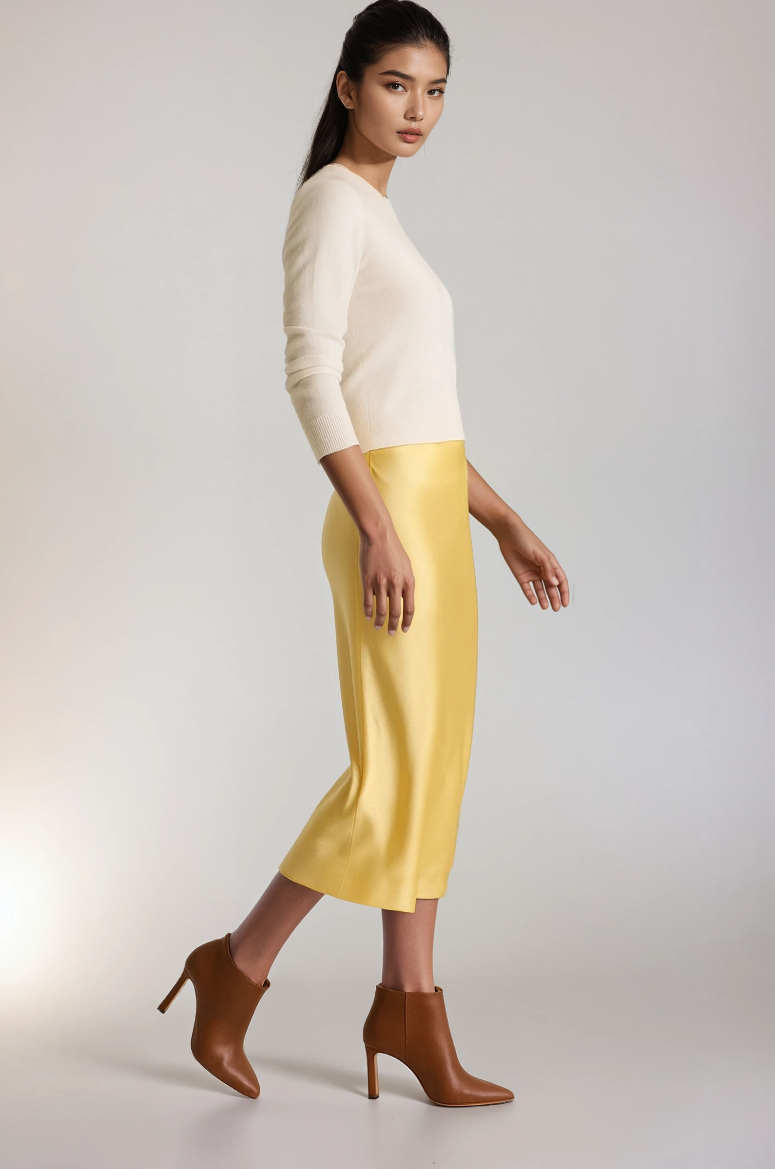 Woman wearing a white top and yellow silk skirt with brown shoes on a plain background