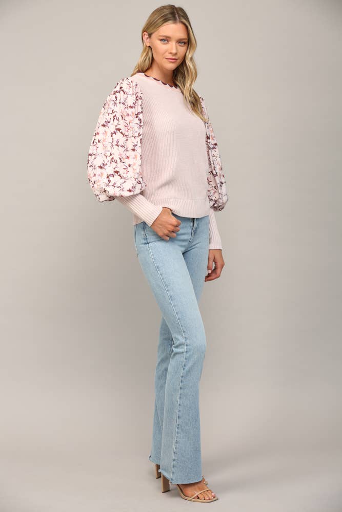 Woman wearing a floral light pink sweater, and light blue jeans on a gray background