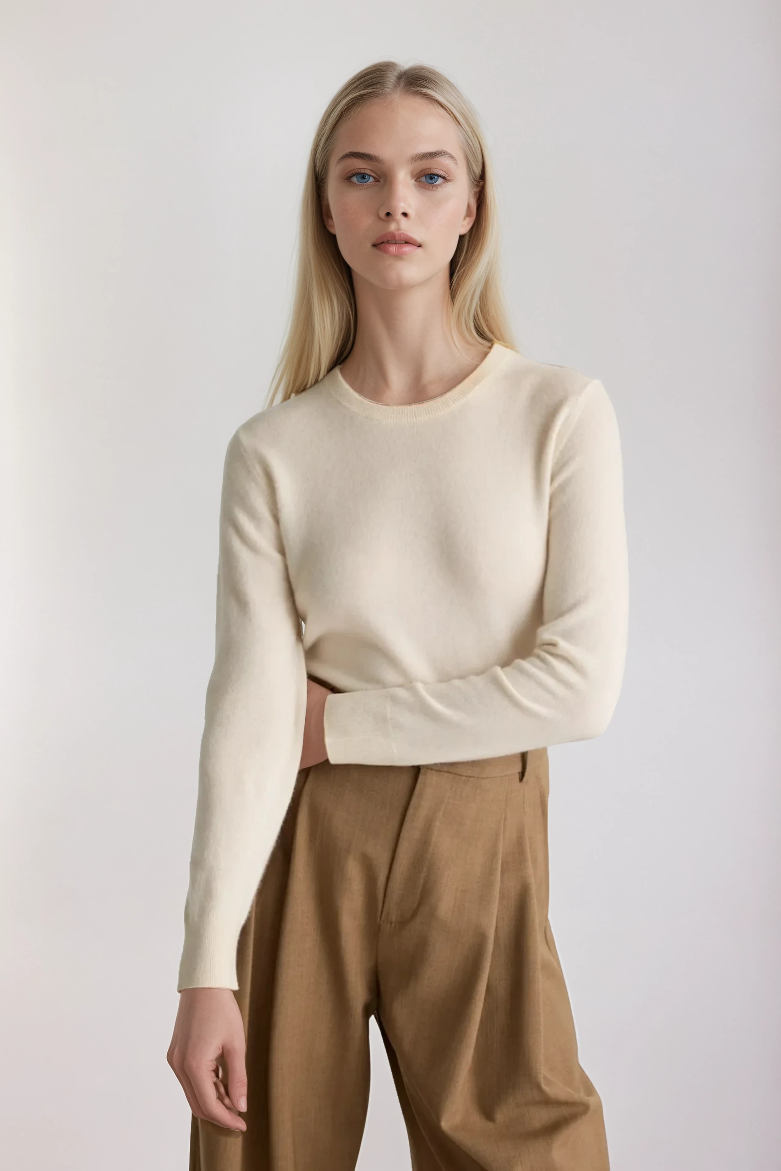 Woman wearing a cream sweater and brown pants against a plain background