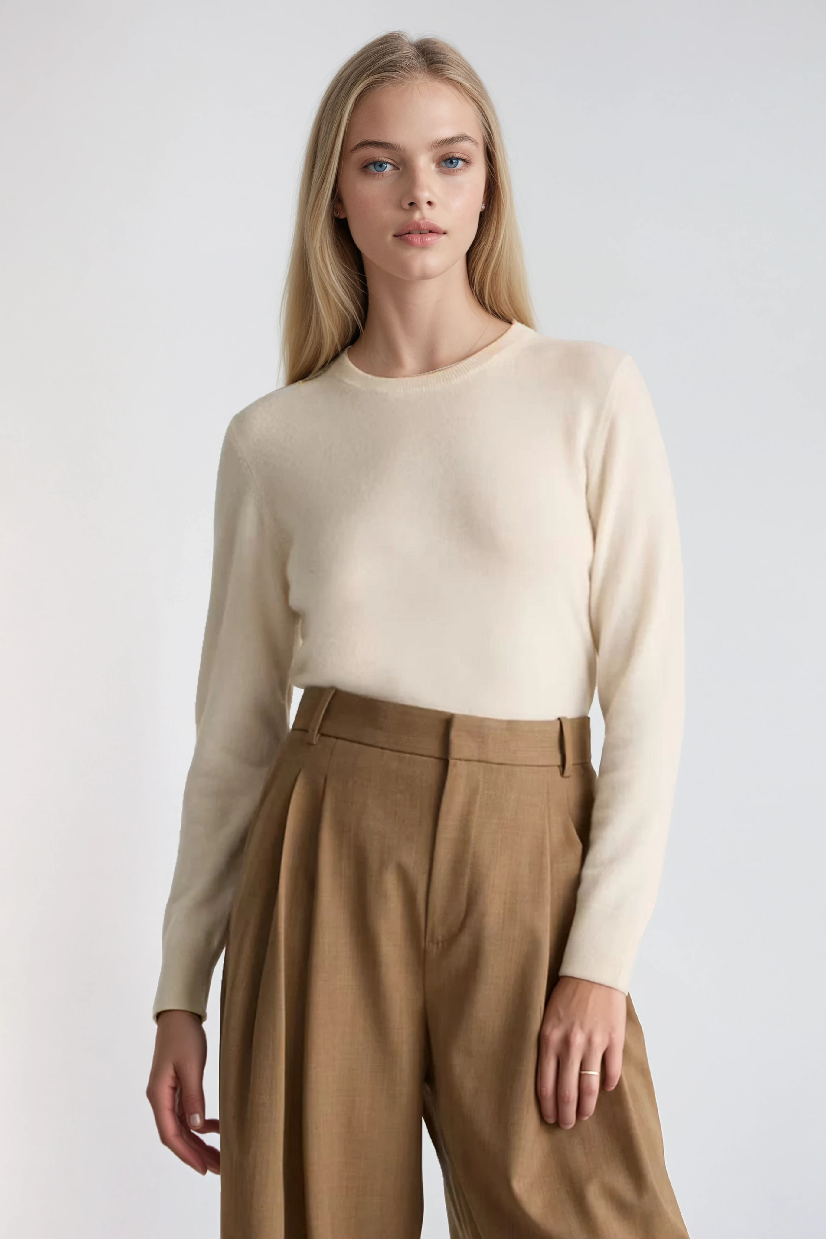 Woman wearing a cream sweater and brown pants on a white background