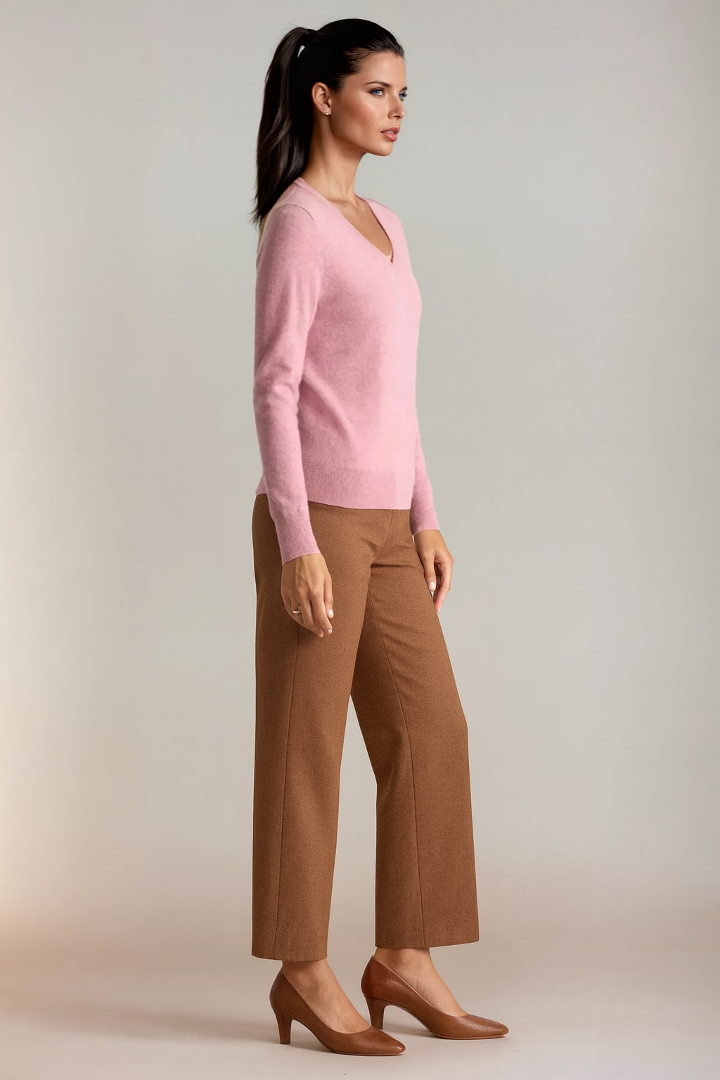 Woman wearing a pink sweater and brown pants against a plain background