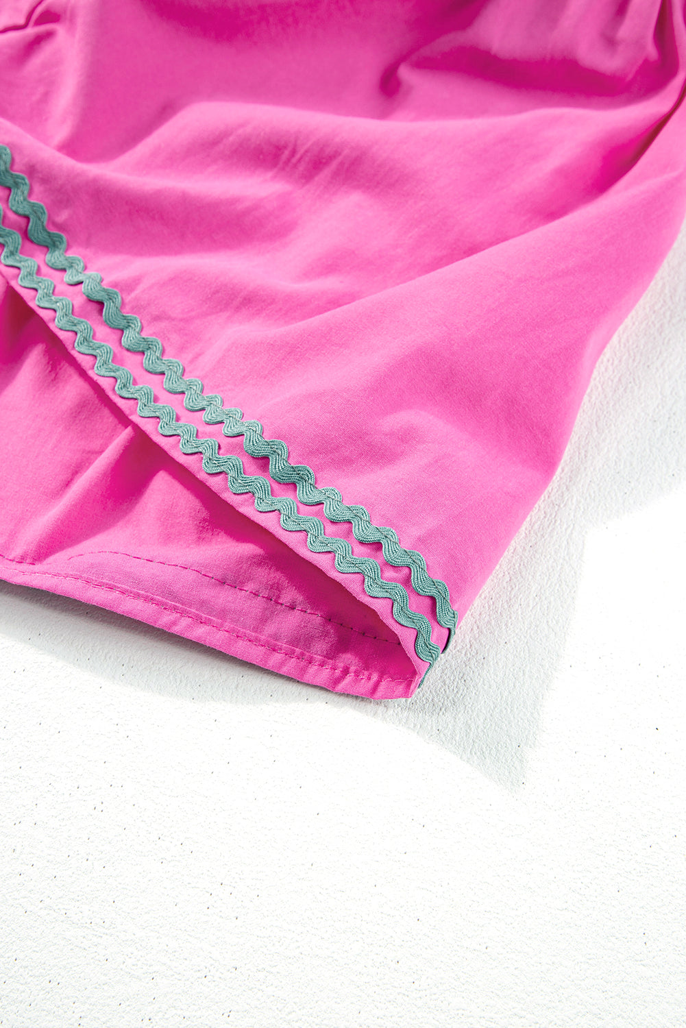 Close-up of a pink garment with green trim on a white background. Women's dress, 100% cotton, cotton dress, summer dress, mini dress.