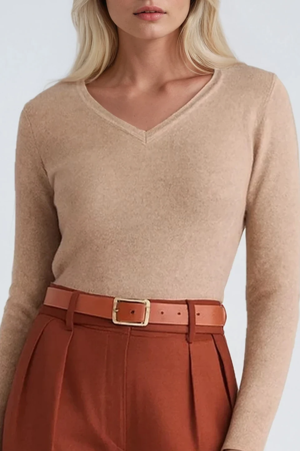 Person wearing a beige sweater and rust-colored pants with a belt on a white background