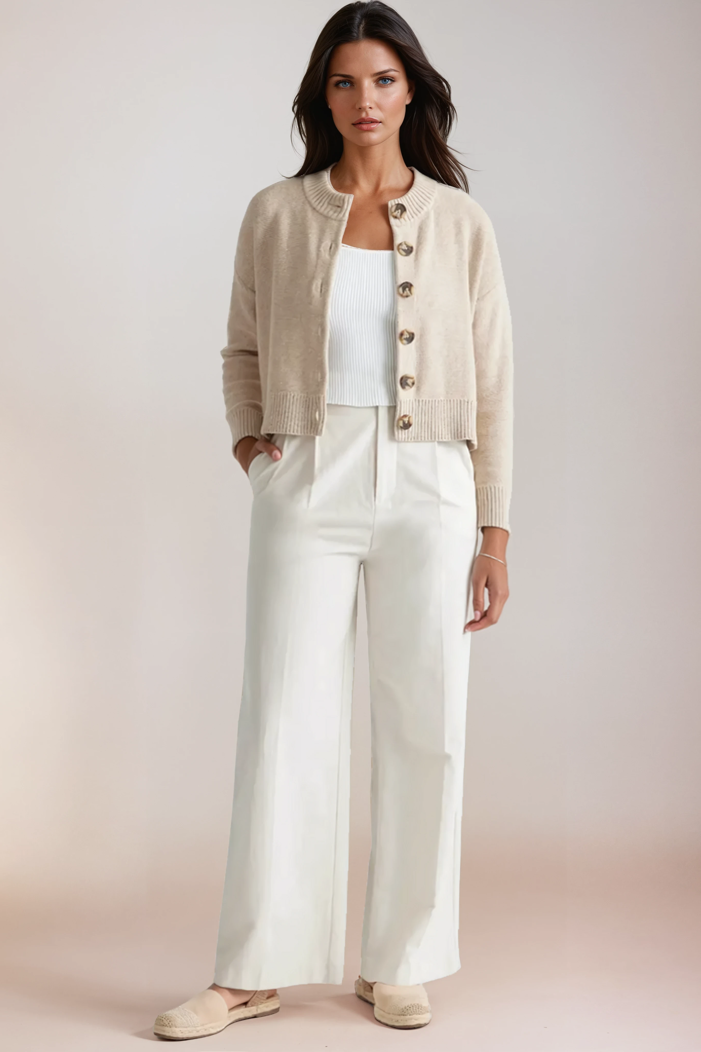 Woman wearing a beige cardigan, white top, and wide-leg pants against a plain background