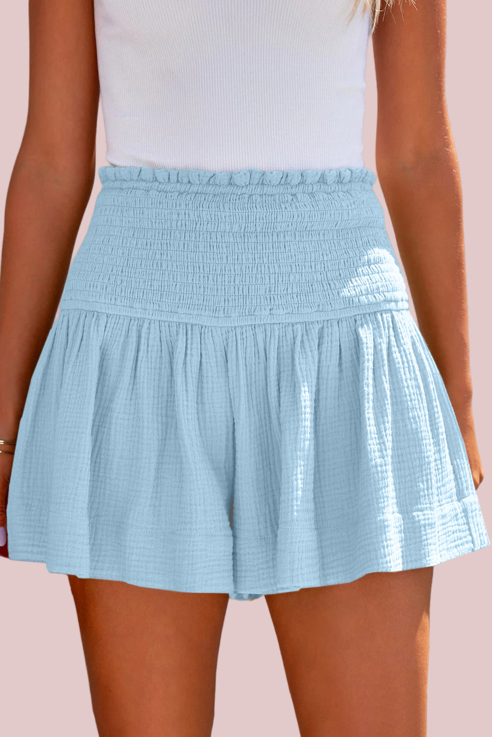 100% Cotton Pastel Blue Smocked Shorts worn by a person on a pink background.