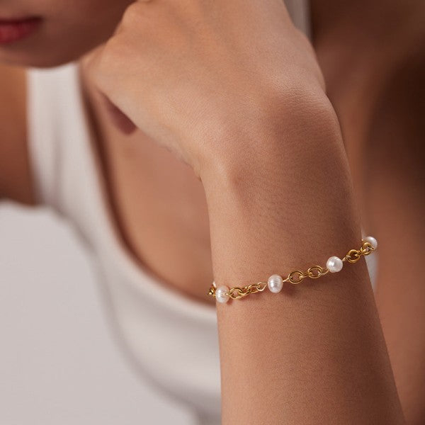 Gold bracelet with pearls on a wrist against a neutral background
