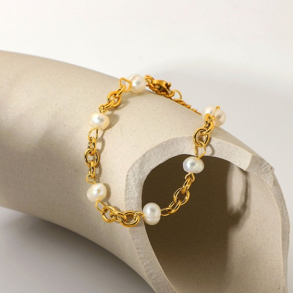 Gold bracelet with pearls on a beige stone surface