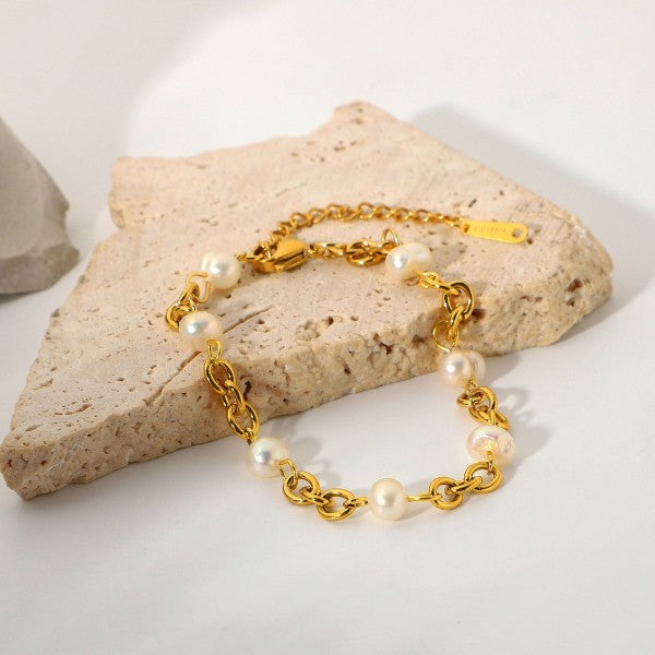 Gold chain bracelet with pearls on a stone surface