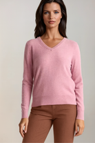 Woman wearing a pink sweater and brown pants against a neutral background