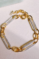 Gold chain bracelet with embedded crystals on a light pink background