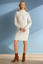 Woman wearing a white wool sweater dress with brown boots against a blue background