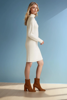 Woman wearing a white sweater dress and brown boots against a light blue background