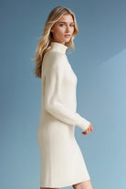 Woman wearing a white ribbed wool sweater dress against a blue background