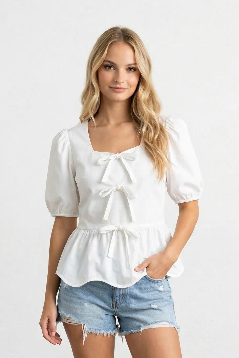 Woman wearing a white blouse and denim shorts against a plain background
