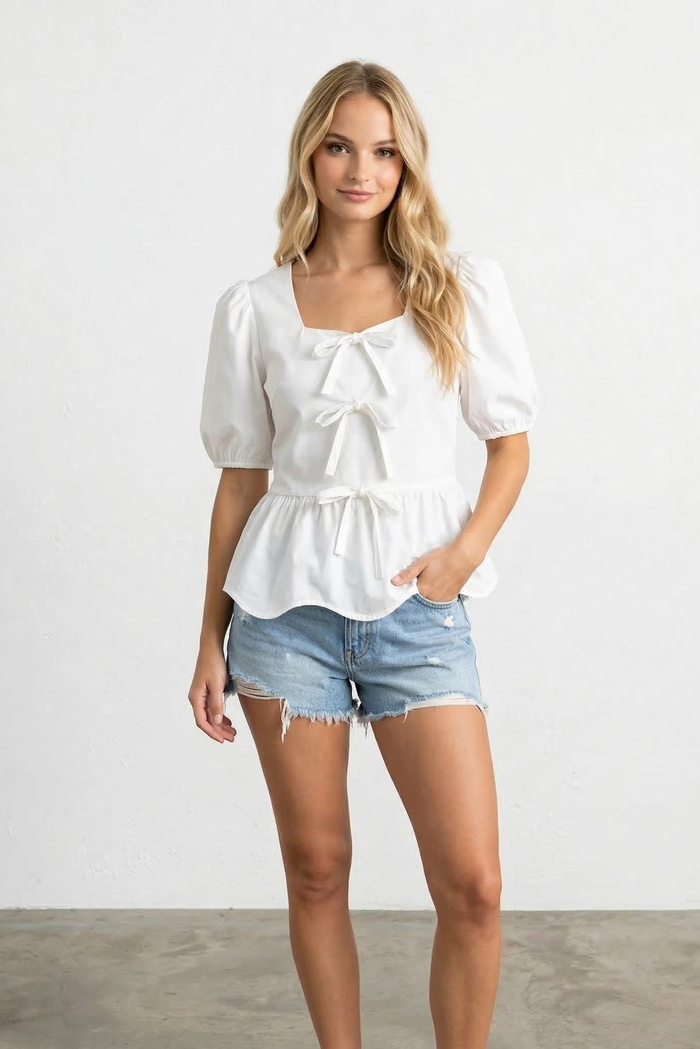 Woman wearing a white blouse and denim shorts against a plain background