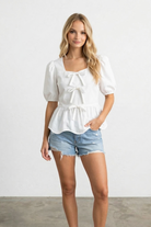 Woman wearing a white blouse and denim shorts against a plain background
