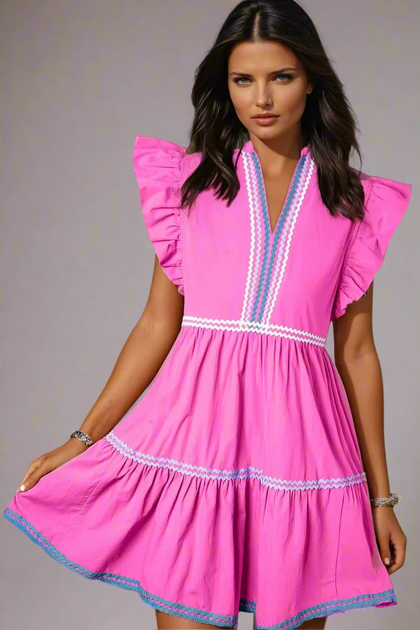 Woman wearing a 100% Cotton Bright Pink Tiered Mini Dress with Ric Rac Trim against a gray background. Women's dress, cotton dress, summer dress, mini dress.